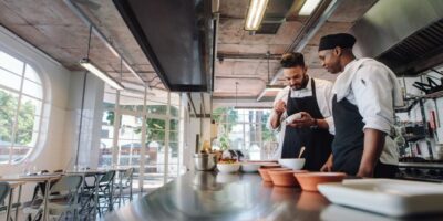 Zwei Köche stehen in einer Gastronomie-Küche und bereiten Mahlzeiten zu.